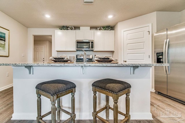 kitchen with light stone counters, a breakfast bar, white cabinetry, appliances with stainless steel finishes, and light wood finished floors