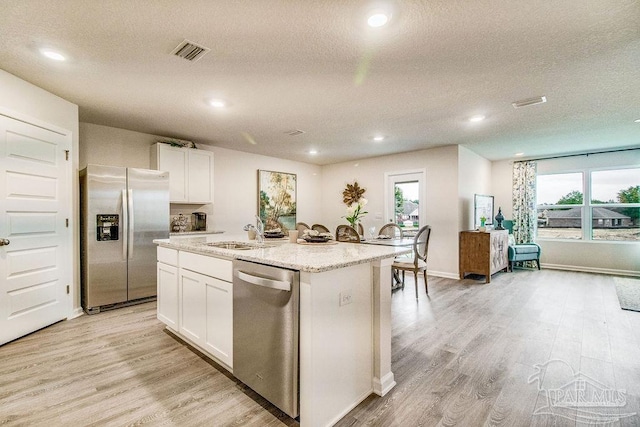 kitchen featuring light wood finished floors, stainless steel appliances, visible vents, a kitchen island with sink, and a sink