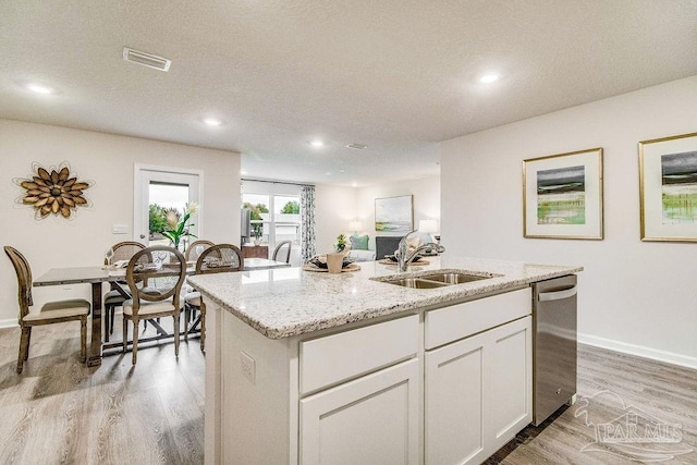 kitchen with a kitchen island with sink, a sink, light wood-style floors, light stone countertops, and dishwasher