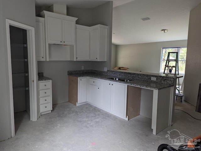 kitchen featuring dark stone countertops, sink, kitchen peninsula, and white cabinets