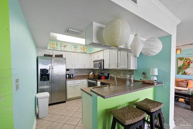 kitchen featuring tasteful backsplash, white cabinets, light tile patterned floors, kitchen peninsula, and stainless steel appliances