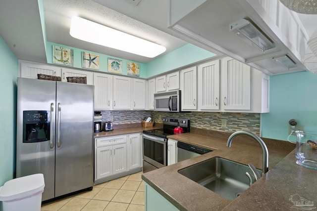 kitchen featuring backsplash, sink, light tile patterned floors, stainless steel appliances, and white cabinets