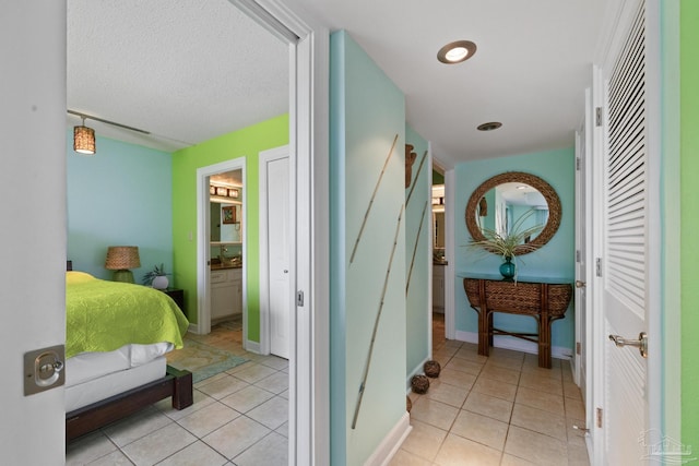 interior space featuring a textured ceiling, light tile patterned flooring, ensuite bath, and baseboards