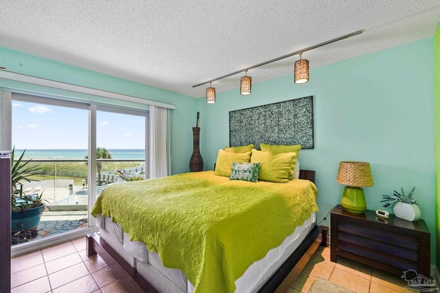 bedroom featuring tile patterned flooring, a water view, a textured ceiling, and track lighting