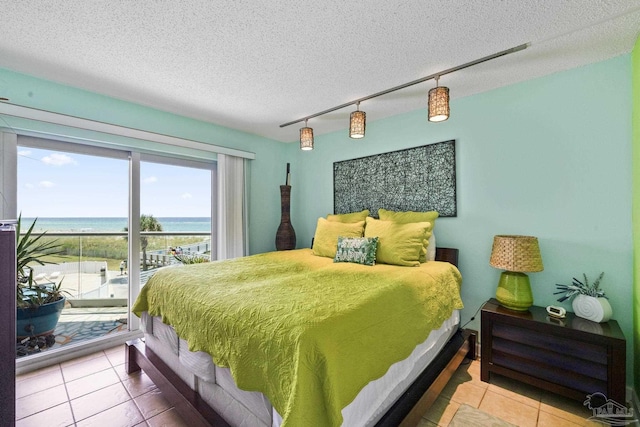 tiled bedroom featuring a water view, access to exterior, track lighting, and a textured ceiling