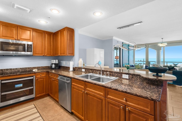 5 Portofino Dr Unit 703, Pensacola Beach, FL 32561 - kitchen featuring stainless steel appliances, brown cabinetry, crown molding, dark stone countertops, and light tile patterned flooring
