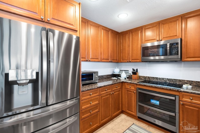 5 Portofino Dr Unit 703, Pensacola Beach, FL 32561 - kitchen with stainless steel appliances, brown cabinets, dark stone counters, light tile patterned floors, and recessed lighting