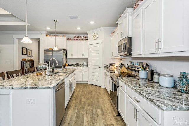 kitchen with a kitchen island with sink, stainless steel appliances, hanging light fixtures, sink, and white cabinetry