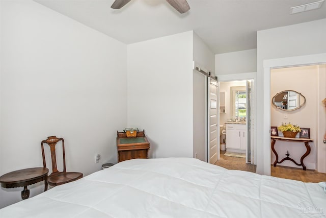 bedroom featuring ceiling fan, connected bathroom, and a barn door