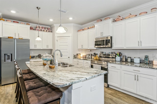 kitchen featuring a kitchen island with sink, appliances with stainless steel finishes, hanging light fixtures, sink, and white cabinetry