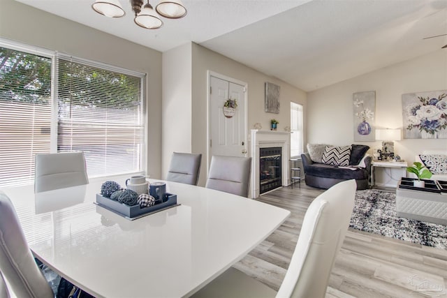 dining space featuring a glass covered fireplace, lofted ceiling, a notable chandelier, and wood finished floors