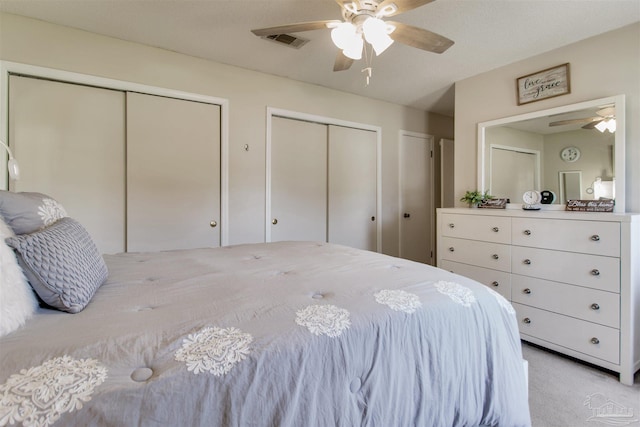 bedroom with a ceiling fan, light colored carpet, visible vents, and two closets