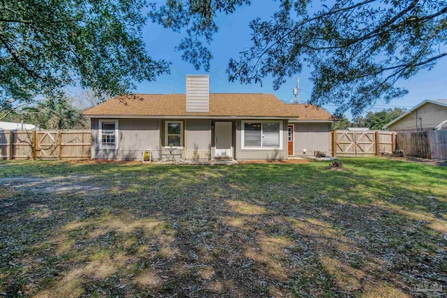 rear view of property featuring a lawn, a fenced backyard, a chimney, and a gate