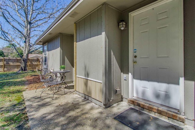 entrance to property with visible vents, a patio, and fence