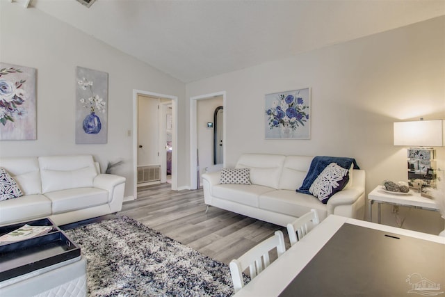 living room with light wood-type flooring, visible vents, and vaulted ceiling