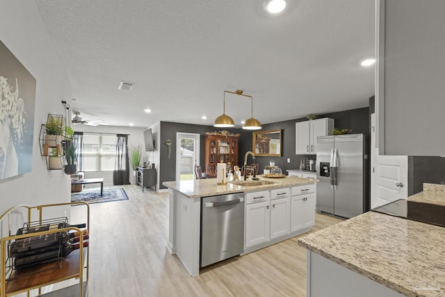 kitchen featuring sink, hanging light fixtures, a center island with sink, stainless steel appliances, and white cabinets