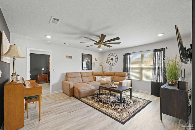 living room with ceiling fan, a textured ceiling, and light wood-type flooring