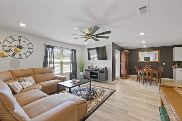 living room featuring ceiling fan, a textured ceiling, and light wood-type flooring