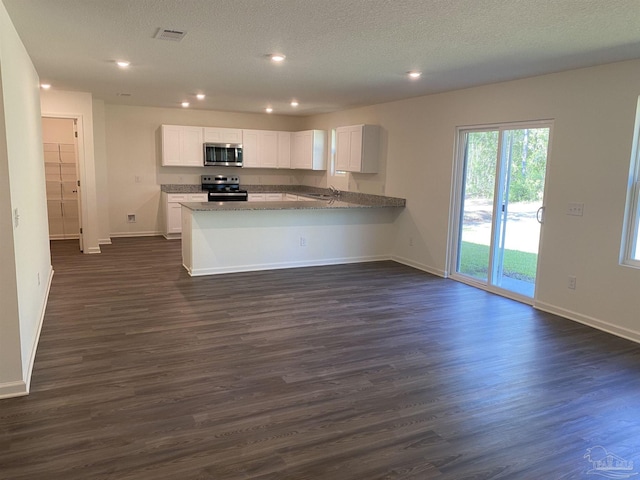 kitchen with dark wood-type flooring, kitchen peninsula, white cabinets, and stainless steel appliances