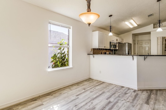 kitchen featuring kitchen peninsula, stainless steel appliances, hanging light fixtures, vaulted ceiling, and white cabinets