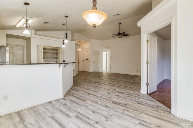 kitchen with pendant lighting, vaulted ceiling, white cabinetry, light wood-type flooring, and ceiling fan