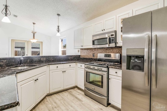 kitchen featuring vaulted ceiling, sink, hanging light fixtures, stainless steel appliances, and white cabinets