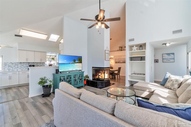 living area with a tile fireplace, visible vents, ceiling fan, and light wood finished floors