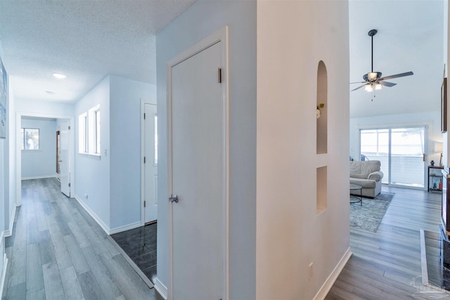 corridor featuring a textured ceiling, wood finished floors, and baseboards