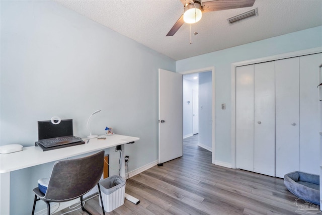 office space featuring visible vents, baseboards, a ceiling fan, light wood-style flooring, and a textured ceiling