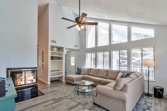 living area featuring a wealth of natural light, visible vents, a textured ceiling, wood finished floors, and a multi sided fireplace