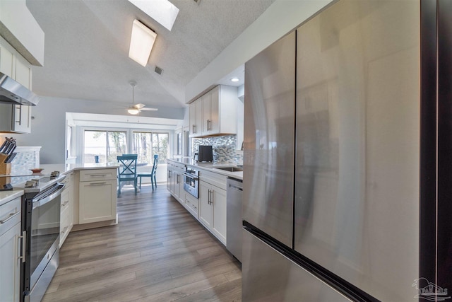 kitchen featuring stainless steel appliances, white cabinets, a peninsula, and decorative backsplash