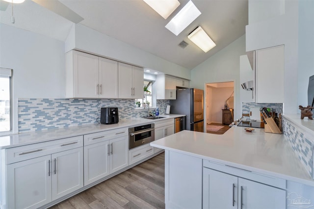 kitchen with stainless steel appliances, tasteful backsplash, lofted ceiling with skylight, white cabinetry, and a sink