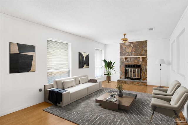 living room featuring hardwood / wood-style floors, ceiling fan, a stone fireplace, and a textured ceiling