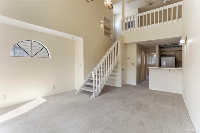 unfurnished living room with a high ceiling, light colored carpet, and ceiling fan