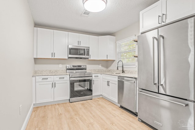 kitchen with sink, stainless steel appliances, a textured ceiling, white cabinets, and light wood-type flooring