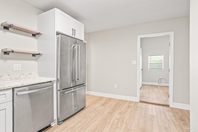 kitchen featuring stainless steel appliances, light stone countertops, a textured ceiling, and white cabinets