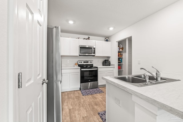 kitchen with appliances with stainless steel finishes, sink, white cabinets, and light wood-type flooring