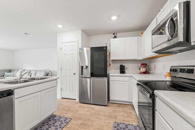 kitchen featuring stainless steel appliances, sink, light hardwood / wood-style flooring, and white cabinets