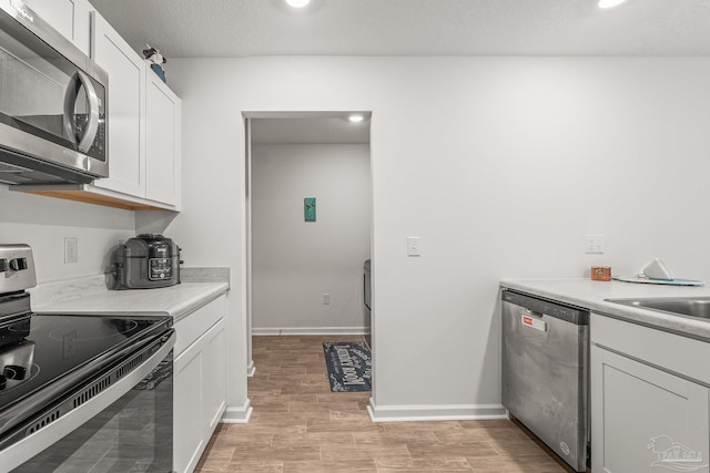 kitchen featuring sink, appliances with stainless steel finishes, a textured ceiling, white cabinets, and light wood-type flooring