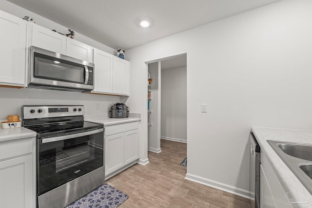 kitchen with sink, appliances with stainless steel finishes, white cabinetry, a textured ceiling, and light wood-type flooring