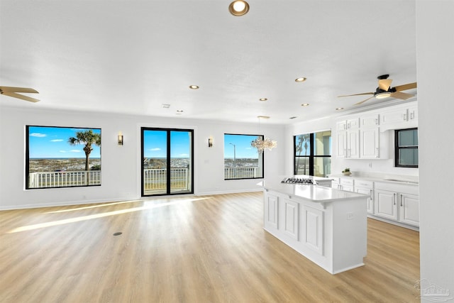 kitchen with ceiling fan with notable chandelier, light hardwood / wood-style flooring, white cabinets, and a kitchen island