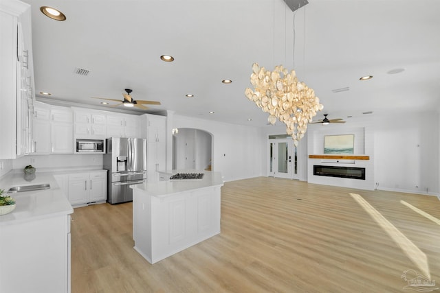 kitchen featuring appliances with stainless steel finishes, white cabinetry, a center island, light hardwood / wood-style floors, and decorative light fixtures