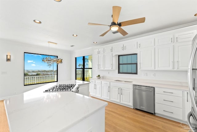 kitchen featuring white cabinetry, decorative light fixtures, light wood-type flooring, stainless steel appliances, and light stone countertops