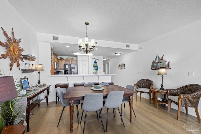 850 Ft Pickens Rd Unit 1230, Pensacola Beach, FL 32561 - dining room with light wood-type flooring, a chandelier, a textured ceiling, and baseboards
