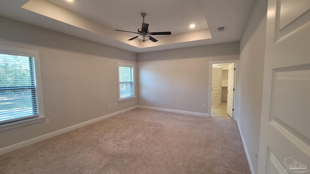 empty room with a tray ceiling, ceiling fan, and light colored carpet