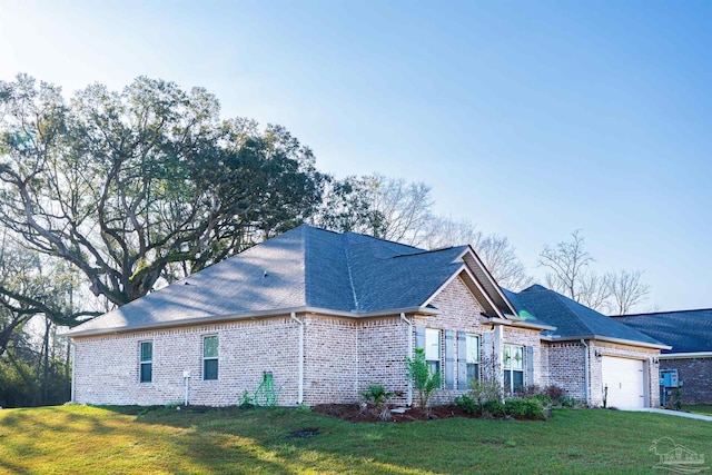 view of side of home with brick siding, a lawn, an attached garage, and roof with shingles