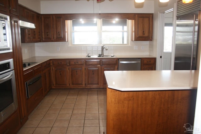 kitchen with tasteful backsplash, sink, built in appliances, light tile patterned floors, and kitchen peninsula