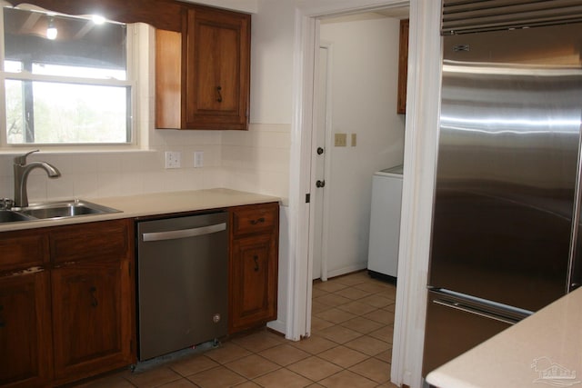 kitchen featuring appliances with stainless steel finishes, tasteful backsplash, washer / clothes dryer, sink, and light tile patterned floors