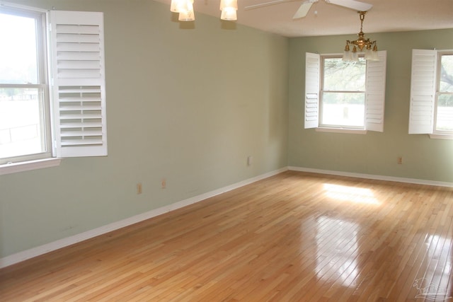 empty room with ceiling fan with notable chandelier and light wood-type flooring