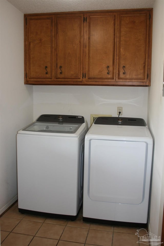 laundry area with cabinets, washer and clothes dryer, a textured ceiling, and light tile patterned floors